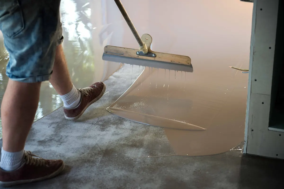Floor installer in spiked shoes spreading a fast-curing coating with a squeegee, leaving a mirror finish