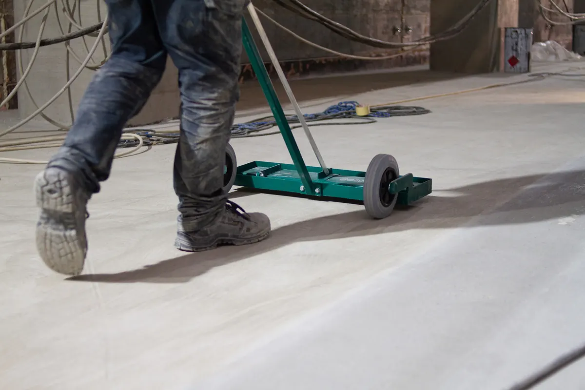 Gray floor coating being spread over a mechanically prepared concrete slab next to a pit