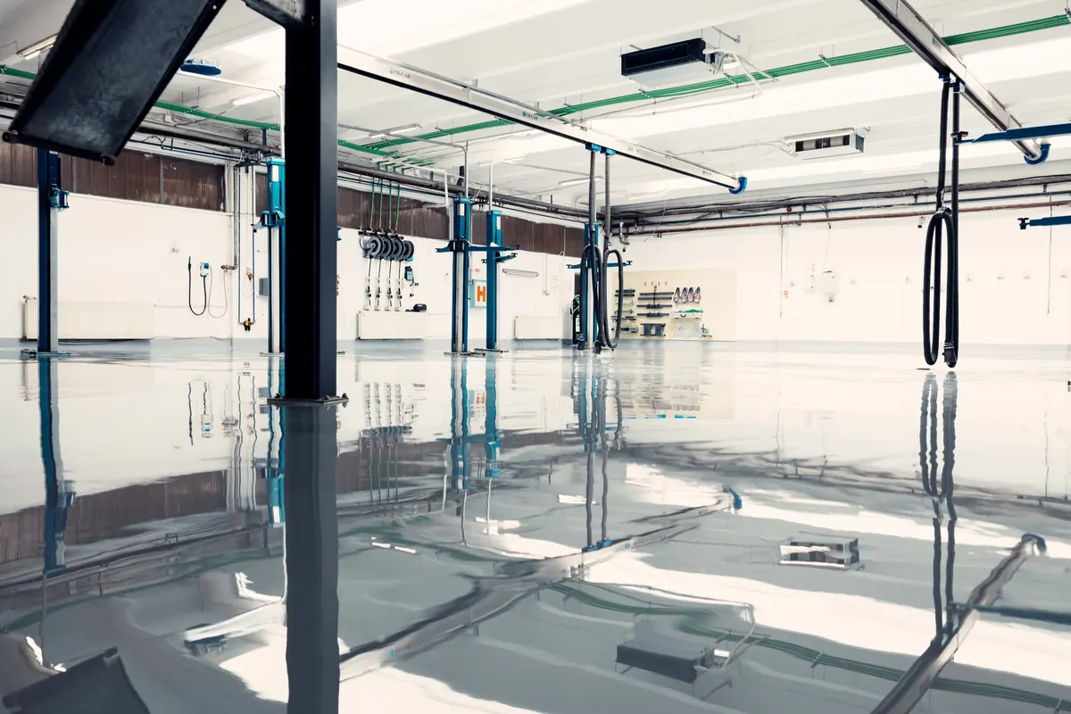 High-gloss light gray epoxy floor in an auto service shop with vehicle lifts reflected in the finish