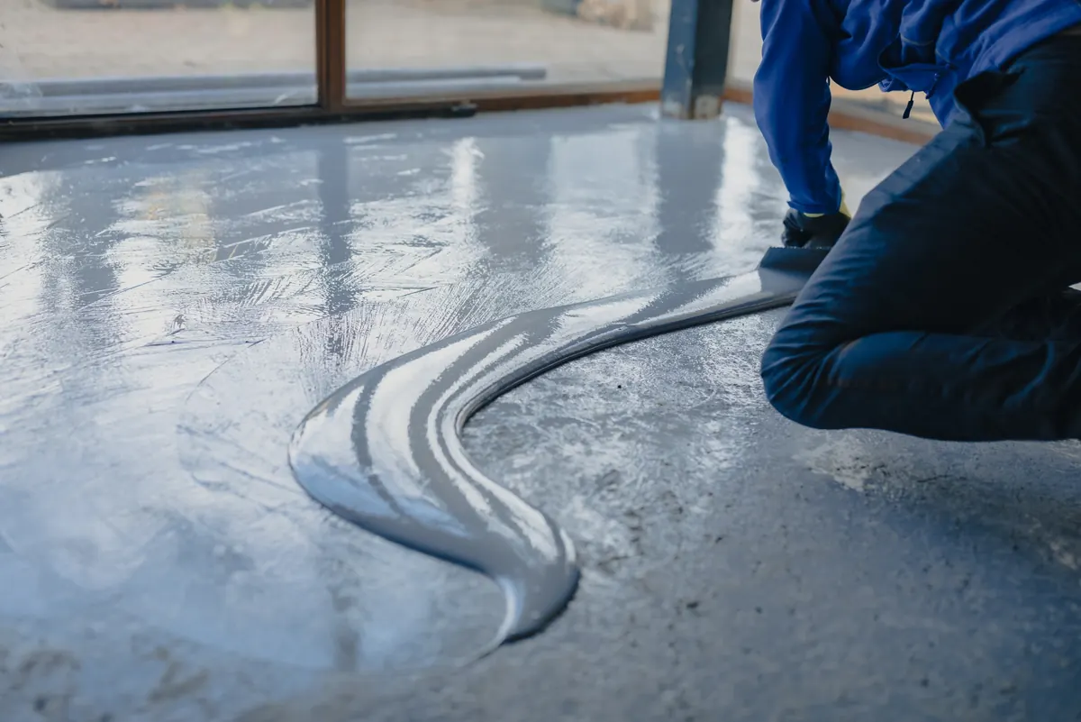 Coating being spread with a squeegee across a floor, reflecting warm light and a column
